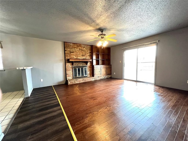 unfurnished living room featuring hardwood / wood-style floors, a fireplace, ceiling fan, a textured ceiling, and built in shelves