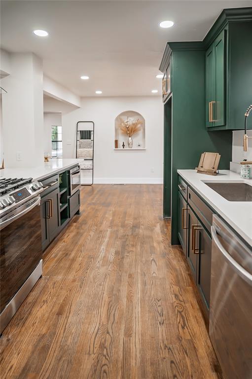 kitchen with sink, stainless steel appliances, light hardwood / wood-style floors, and green cabinetry