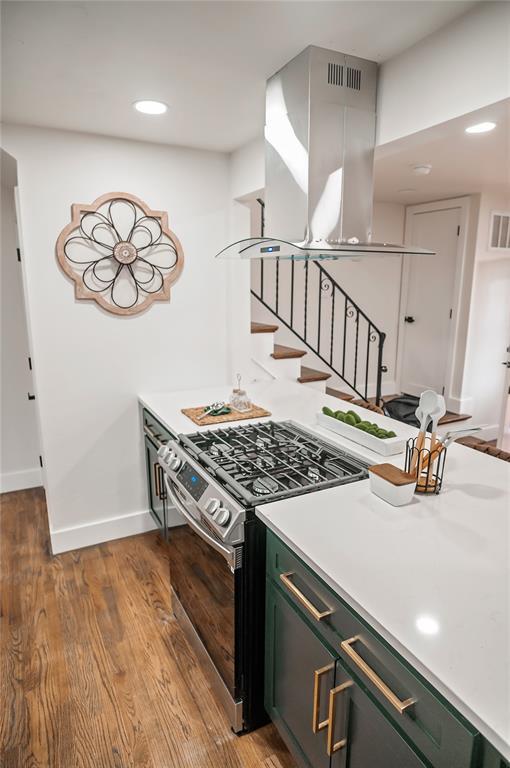 kitchen with island exhaust hood, stainless steel range with gas cooktop, light wood-type flooring, and green cabinetry