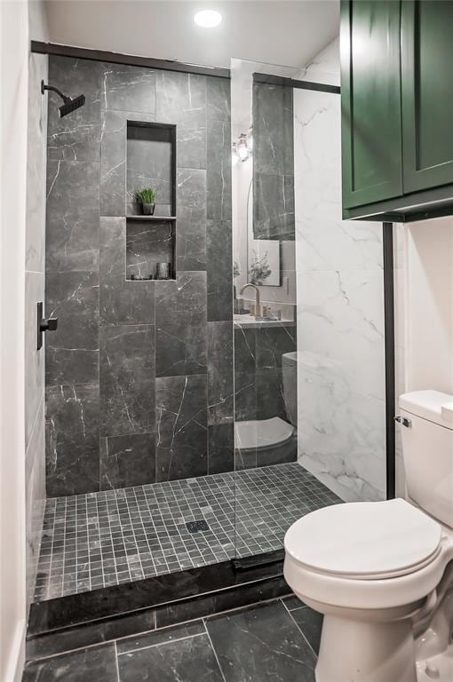 bathroom with sink, a tile shower, and toilet