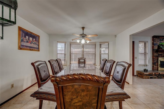 dining space with a brick fireplace, light tile patterned floors, and ceiling fan