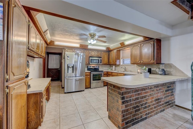 kitchen with appliances with stainless steel finishes, a tray ceiling, sink, light tile patterned floors, and kitchen peninsula