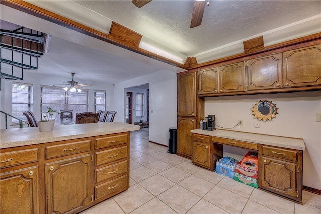 kitchen with light tile patterned floors, ceiling fan, built in desk, a textured ceiling, and a raised ceiling