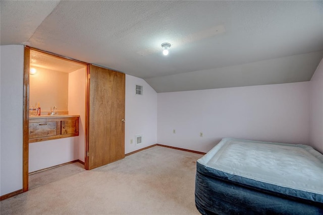 bedroom featuring vaulted ceiling, light colored carpet, and a textured ceiling