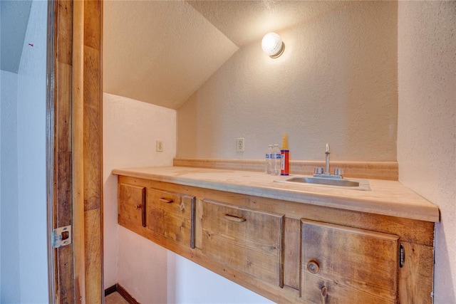 bathroom featuring vaulted ceiling, sink, and a textured ceiling