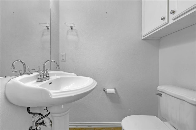 half bath featuring a textured wall, baseboards, a sink, and toilet