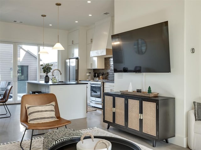 kitchen with pendant lighting, white cabinets, custom exhaust hood, a kitchen island with sink, and stainless steel appliances