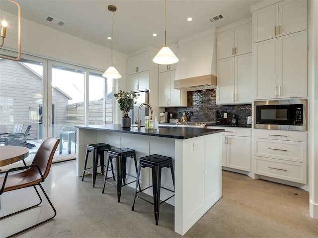 kitchen with a kitchen island with sink, hanging light fixtures, white cabinets, built in microwave, and custom exhaust hood