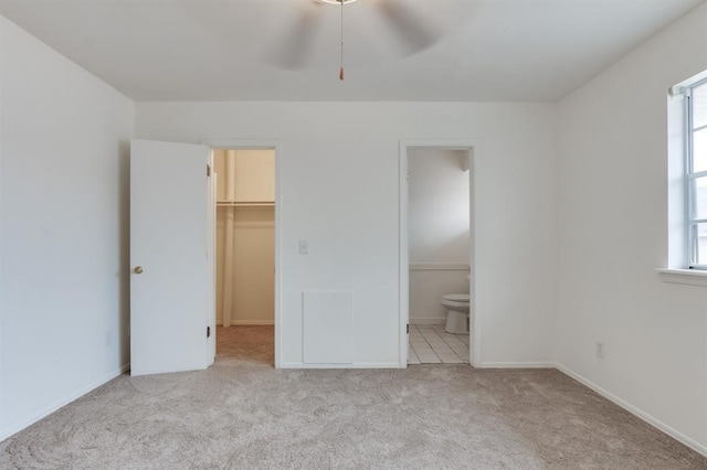 unfurnished bedroom featuring multiple windows, ensuite bathroom, a walk in closet, and light carpet