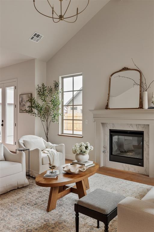 living room featuring a premium fireplace, vaulted ceiling, hardwood / wood-style floors, and an inviting chandelier