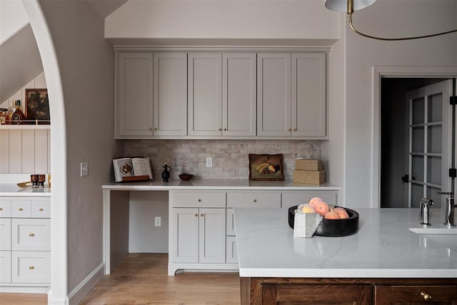 bar featuring light stone counters, tasteful backsplash, and light wood-type flooring