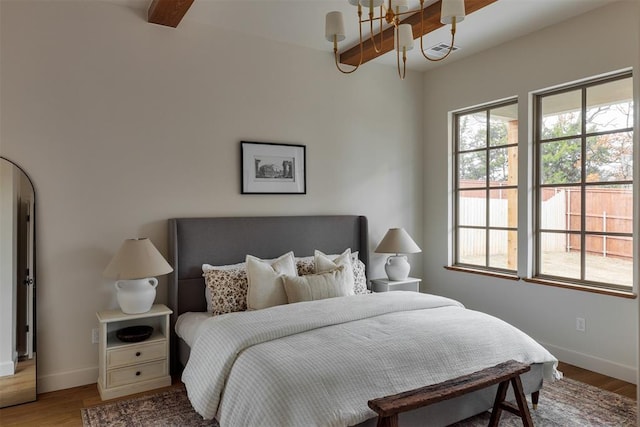 bedroom with beamed ceiling, wood-type flooring, and a chandelier