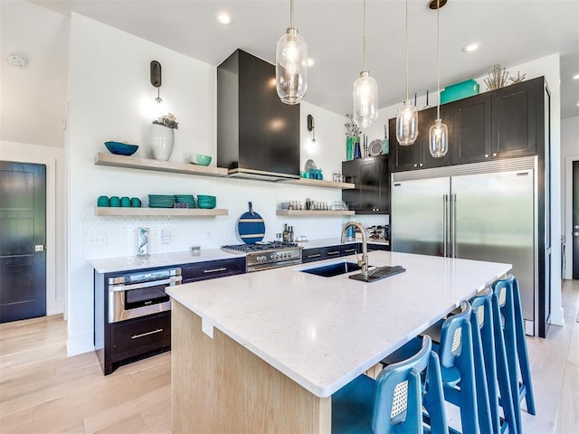 kitchen with wall chimney exhaust hood, a center island with sink, open shelves, and premium appliances