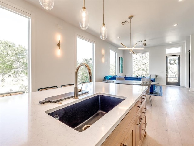 kitchen featuring visible vents, open floor plan, hanging light fixtures, light brown cabinets, and a sink