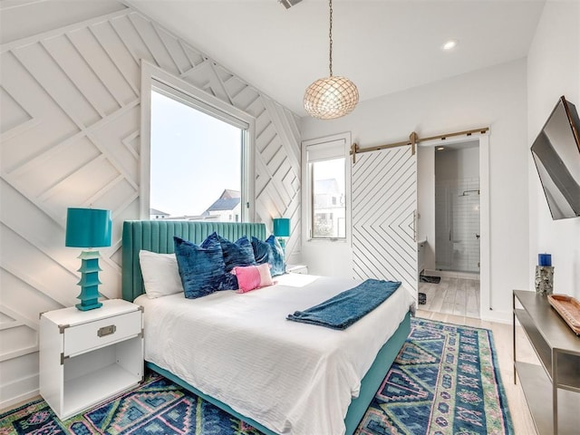 bedroom with a barn door, connected bathroom, and light wood-type flooring