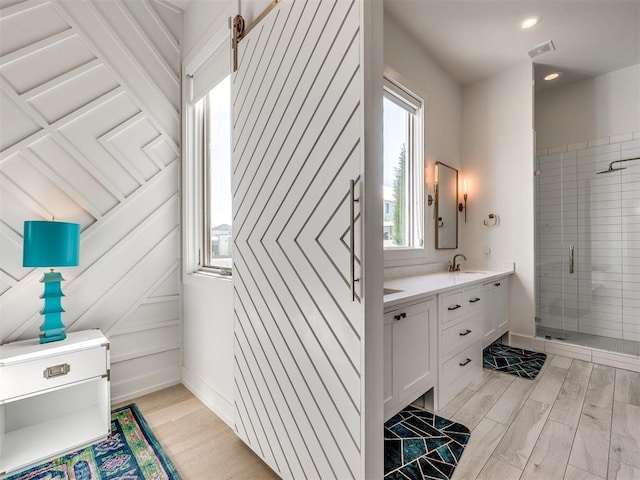 bathroom with double vanity, a sink, wood finished floors, and a shower stall