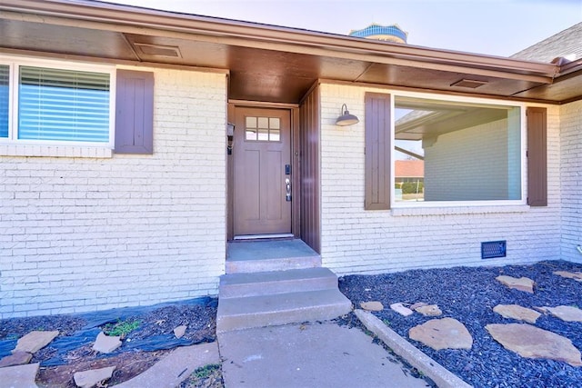 view of exterior entry with brick siding and crawl space