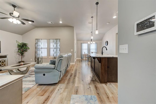 living room featuring sink, ceiling fan with notable chandelier, vaulted ceiling, and light wood-type flooring