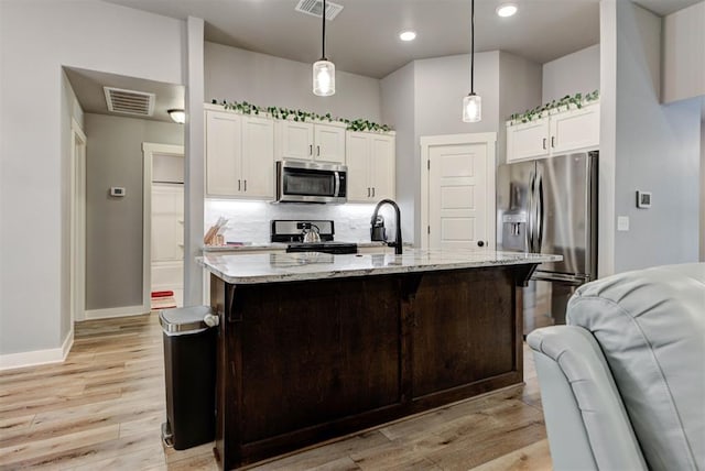 kitchen featuring a center island with sink, hanging light fixtures, appliances with stainless steel finishes, light stone countertops, and white cabinets