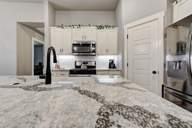 kitchen with decorative backsplash, light stone countertops, white cabinets, and appliances with stainless steel finishes