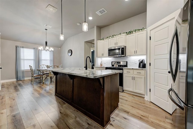 kitchen featuring white cabinetry, hanging light fixtures, a center island with sink, stainless steel appliances, and light stone countertops