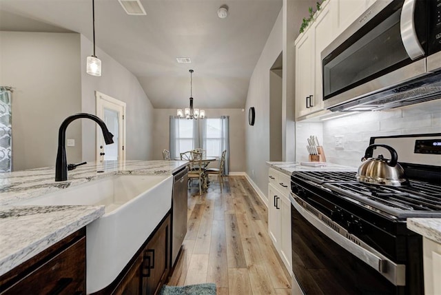 kitchen featuring dark brown cabinetry, lofted ceiling, white cabinetry, hanging light fixtures, and stainless steel appliances