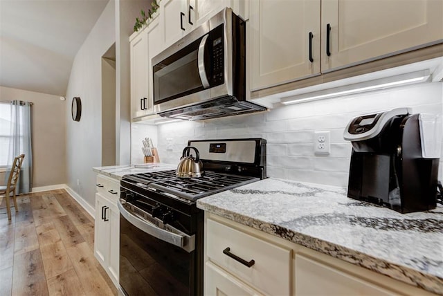 kitchen with vaulted ceiling, decorative backsplash, light stone countertops, gas range oven, and light hardwood / wood-style flooring