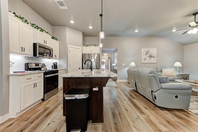 kitchen with decorative light fixtures, a center island with sink, appliances with stainless steel finishes, light stone countertops, and white cabinets