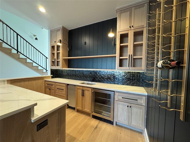 kitchen featuring wine cooler, tasteful backsplash, light wood-style flooring, glass insert cabinets, and a sink