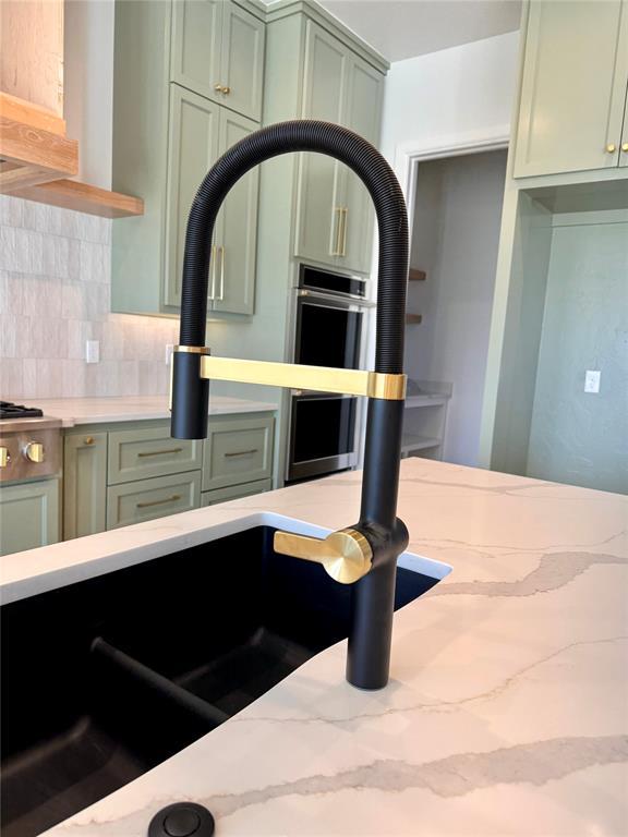 kitchen featuring a sink, light stone countertops, decorative backsplash, and green cabinetry