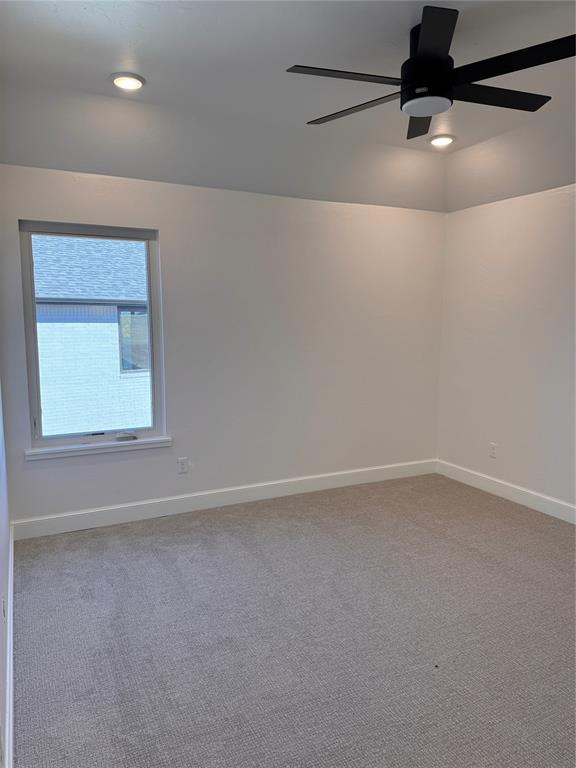 carpeted spare room featuring ceiling fan and baseboards