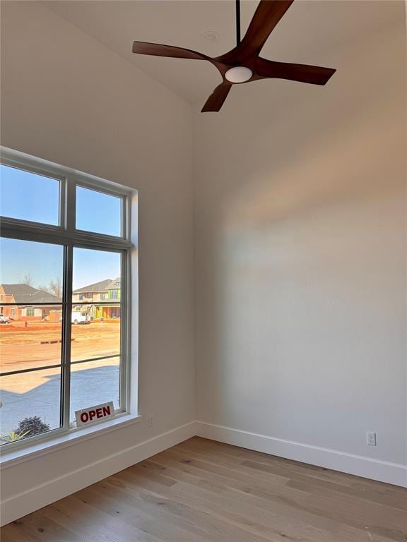 unfurnished room with a residential view, ceiling fan, light wood-style flooring, and baseboards