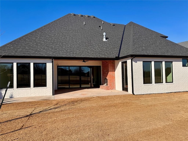 rear view of property with brick siding, a shingled roof, a yard, and a patio