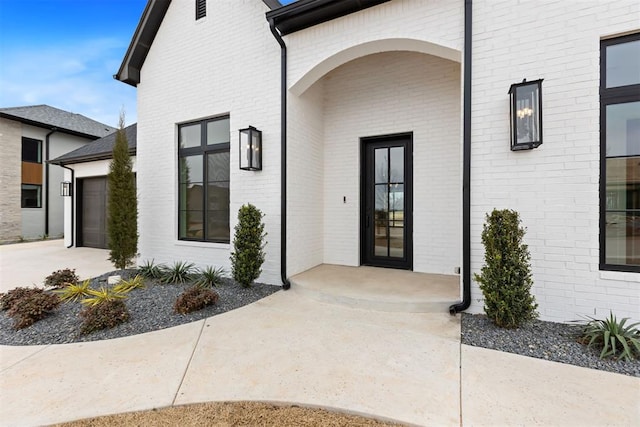 property entrance with brick siding, driveway, and a garage