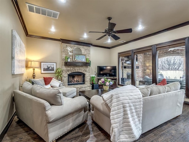 living room with dark wood-type flooring, ceiling fan, crown molding, and a stone fireplace