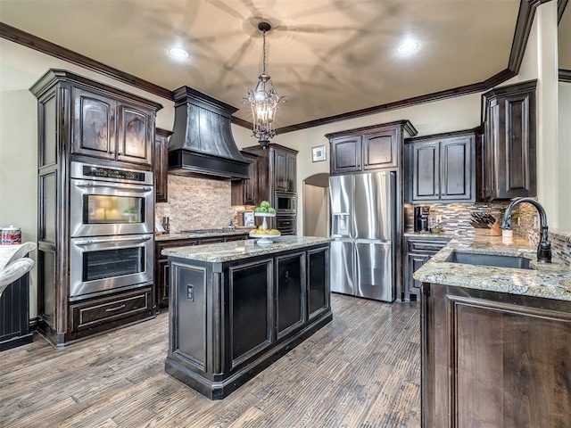 kitchen with sink, light stone counters, a kitchen island, custom range hood, and stainless steel appliances