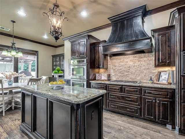 kitchen featuring pendant lighting, an inviting chandelier, dark brown cabinets, a center island, and custom exhaust hood