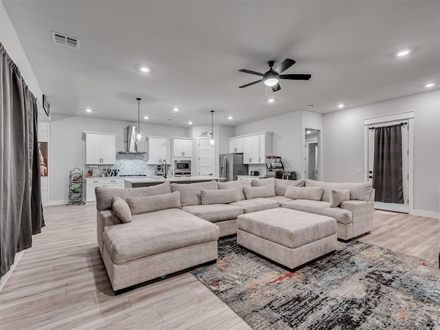 living room with ceiling fan, sink, and light wood-type flooring