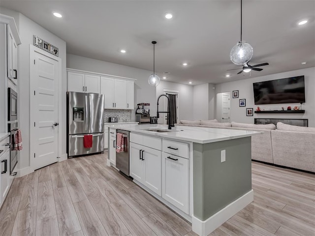 kitchen featuring sink, white cabinetry, appliances with stainless steel finishes, pendant lighting, and a kitchen island with sink