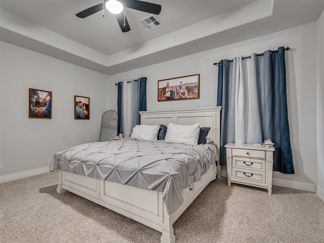 carpeted bedroom with a raised ceiling and ceiling fan