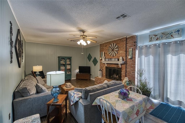 living room featuring hardwood / wood-style flooring, a brick fireplace, a textured ceiling, and ceiling fan