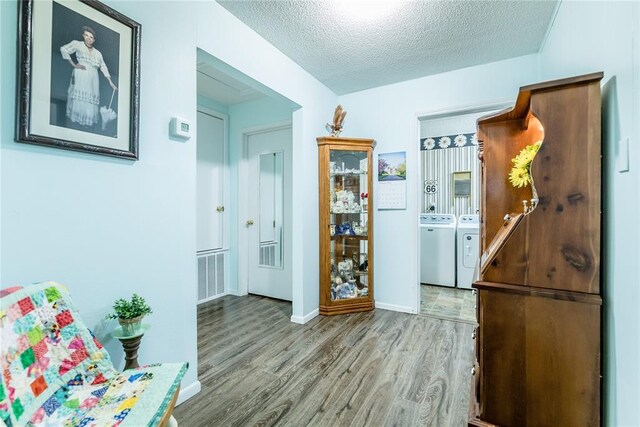 corridor with washer and dryer, a textured ceiling, and light hardwood / wood-style flooring