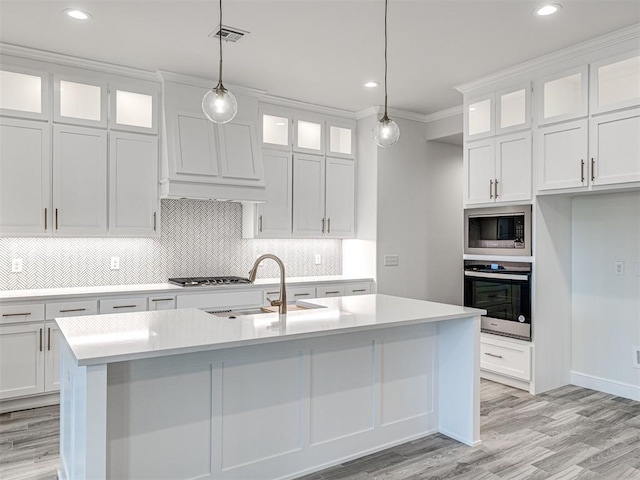 kitchen featuring appliances with stainless steel finishes, sink, white cabinets, hanging light fixtures, and a kitchen island with sink