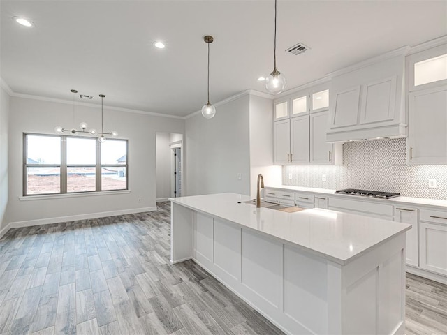 kitchen with sink, stainless steel gas stovetop, an island with sink, and white cabinets