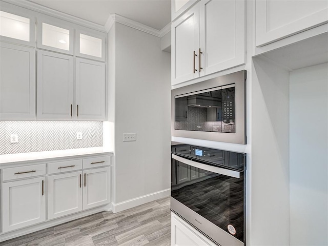 kitchen featuring white cabinetry, tasteful backsplash, ornamental molding, stainless steel appliances, and light hardwood / wood-style floors