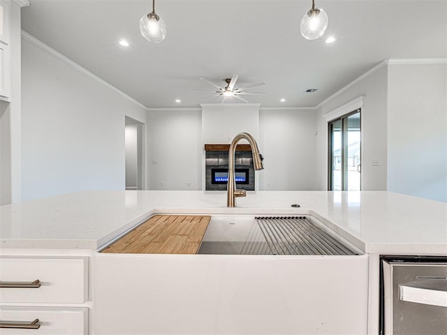 kitchen with white cabinetry, ornamental molding, a fireplace, and hanging light fixtures