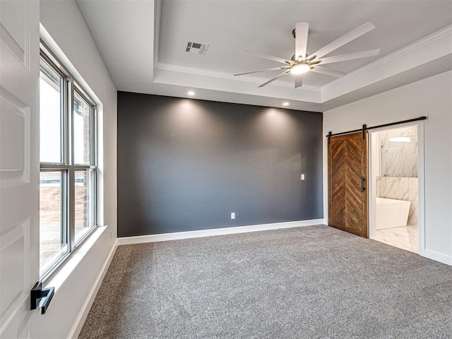 carpeted spare room featuring a barn door, ceiling fan, a healthy amount of sunlight, and a tray ceiling