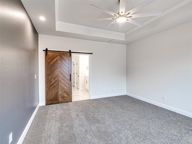 unfurnished bedroom with a barn door, ornamental molding, a raised ceiling, and carpet flooring