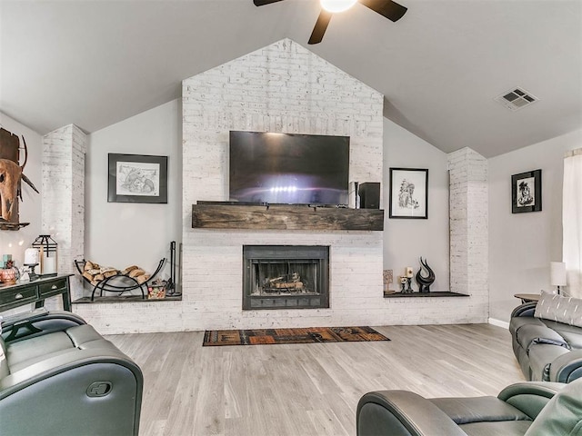 living area featuring lofted ceiling, a large fireplace, visible vents, and wood finished floors