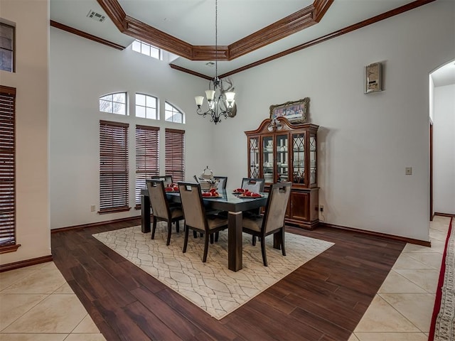 dining space featuring crown molding, a notable chandelier, a high ceiling, and light wood-type flooring